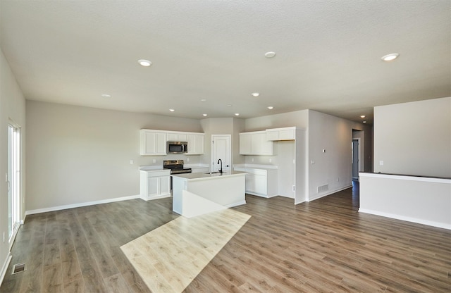 kitchen with appliances with stainless steel finishes, sink, white cabinets, hardwood / wood-style floors, and an island with sink