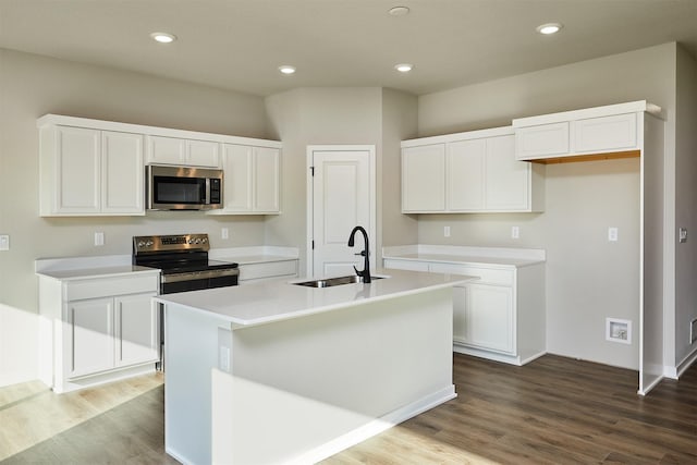 kitchen featuring hardwood / wood-style floors, white cabinetry, sink, stainless steel appliances, and a center island with sink