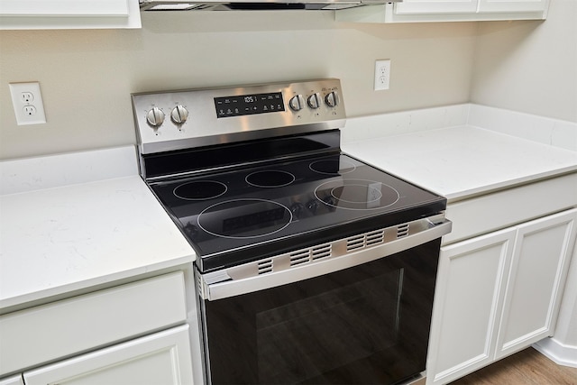 kitchen featuring stainless steel electric stove, white cabinets, and ventilation hood