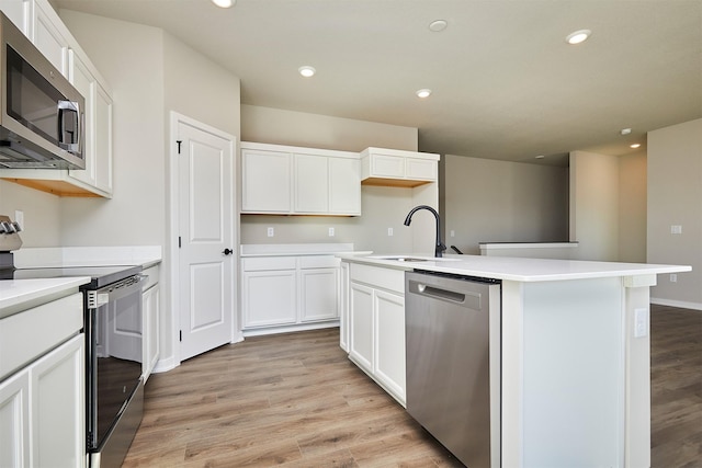 kitchen featuring appliances with stainless steel finishes, white cabinetry, an island with sink, sink, and light hardwood / wood-style flooring