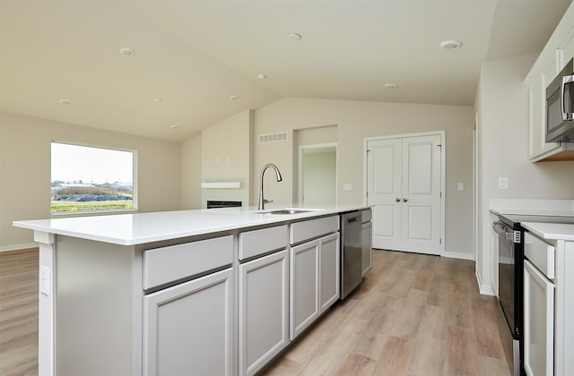 kitchen featuring light wood-type flooring, appliances with stainless steel finishes, sink, an island with sink, and vaulted ceiling