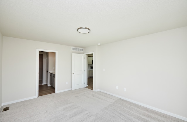 unfurnished bedroom with ensuite bathroom, a textured ceiling, and light carpet