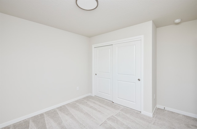 unfurnished bedroom featuring light colored carpet, a textured ceiling, and a closet