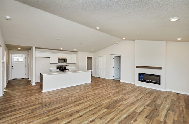 unfurnished living room with vaulted ceiling, light hardwood / wood-style flooring, a textured ceiling, and sink