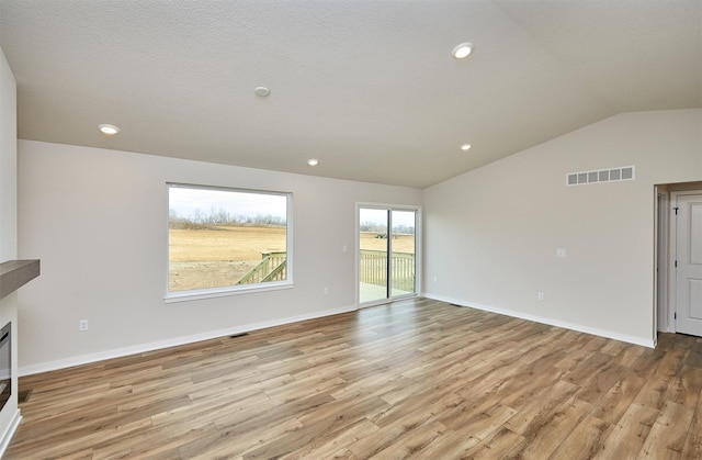 unfurnished living room with light hardwood / wood-style floors, a textured ceiling, and vaulted ceiling