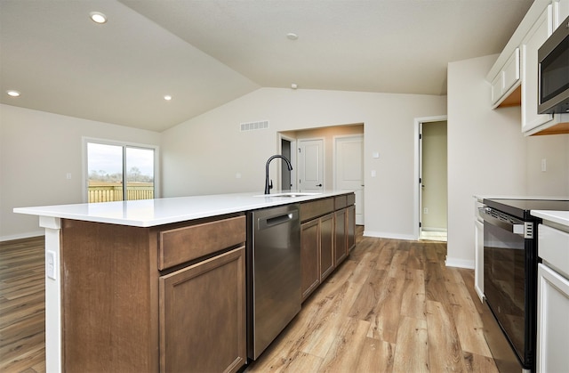 kitchen featuring light wood-type flooring, stainless steel appliances, vaulted ceiling, a kitchen island with sink, and sink