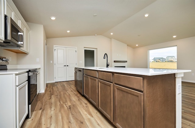 kitchen featuring stainless steel appliances, vaulted ceiling, a center island with sink, light hardwood / wood-style flooring, and white cabinets