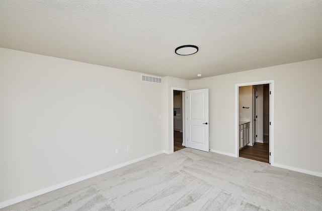 unfurnished bedroom with ensuite bathroom, light carpet, and a textured ceiling