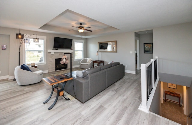 living room featuring a fireplace, a raised ceiling, ceiling fan, and light hardwood / wood-style floors