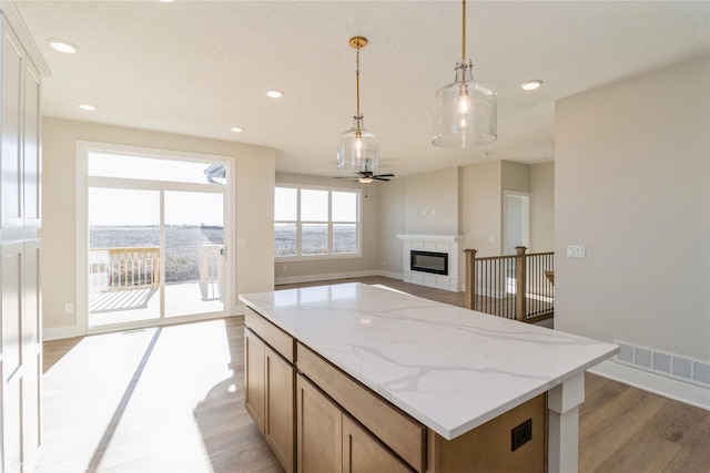 kitchen with pendant lighting, a tile fireplace, ceiling fan, light hardwood / wood-style floors, and light stone counters