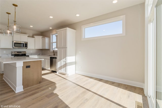 kitchen with appliances with stainless steel finishes, pendant lighting, light hardwood / wood-style flooring, white cabinets, and a center island