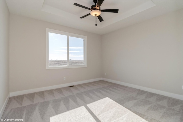 carpeted spare room featuring ceiling fan and a raised ceiling