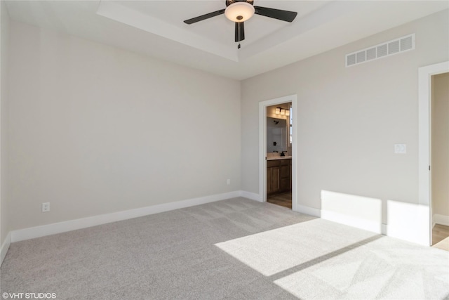 unfurnished bedroom featuring a raised ceiling, ceiling fan, light colored carpet, and connected bathroom