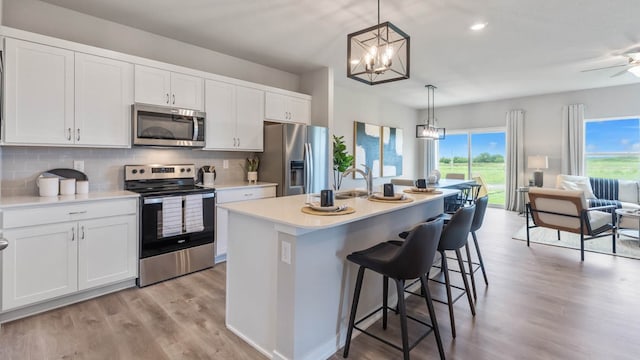 kitchen with pendant lighting, stainless steel appliances, white cabinetry, and an island with sink