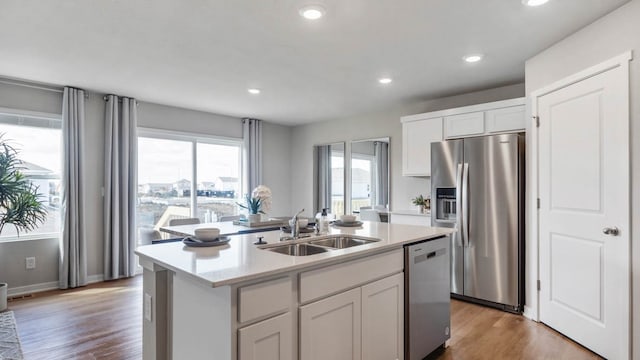 kitchen with an island with sink, stainless steel appliances, white cabinetry, and sink