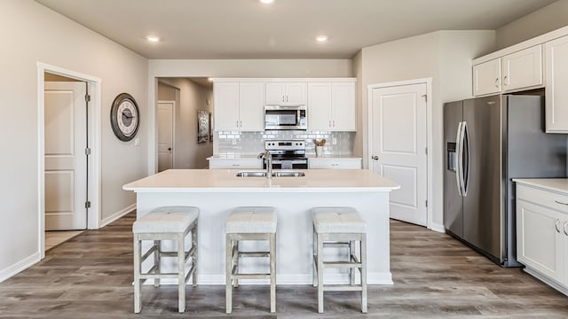 kitchen with hardwood / wood-style floors, a center island with sink, white cabinets, tasteful backsplash, and stainless steel appliances