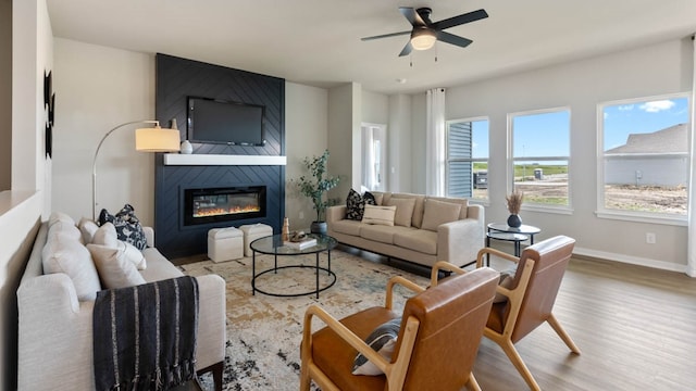 living room featuring ceiling fan, a large fireplace, and hardwood / wood-style flooring