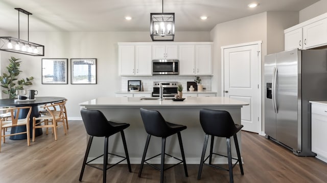 kitchen featuring dark hardwood / wood-style flooring, stainless steel appliances, a kitchen island with sink, white cabinets, and hanging light fixtures