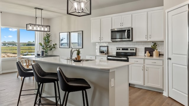 kitchen with appliances with stainless steel finishes, decorative light fixtures, white cabinetry, and an island with sink