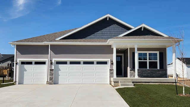 view of front of home with stone siding, a front yard, covered porch, and an attached garage