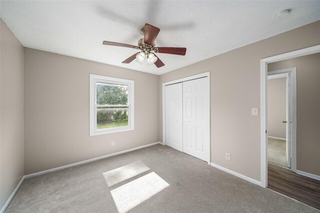 unfurnished bedroom with a closet, carpet floors, a textured ceiling, baseboards, and ceiling fan