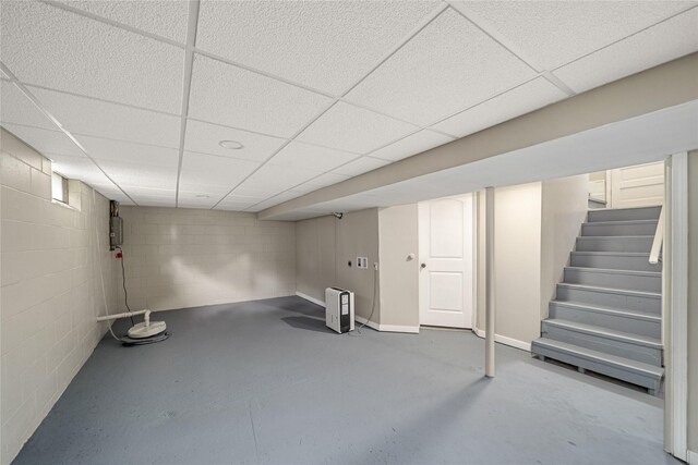 finished below grade area with concrete block wall, stairway, and a paneled ceiling