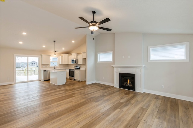 unfurnished living room with light wood-type flooring, vaulted ceiling, ceiling fan, and sink