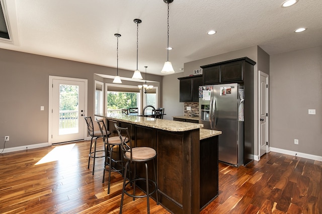 kitchen with a kitchen breakfast bar, light stone counters, dark hardwood / wood-style flooring, decorative light fixtures, and stainless steel fridge with ice dispenser