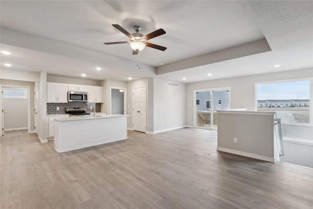 kitchen with white cabinetry, appliances with stainless steel finishes, an island with sink, and light wood-type flooring