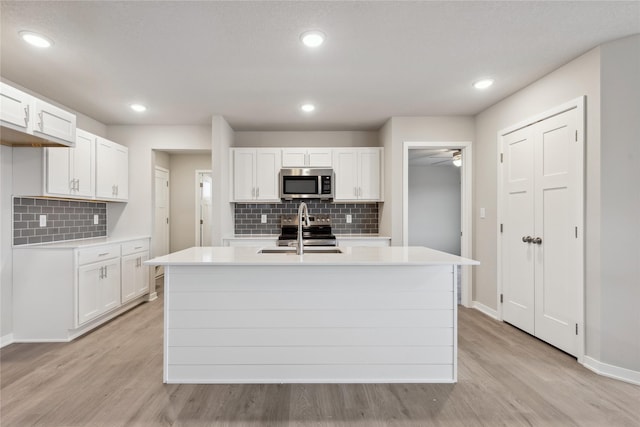 kitchen featuring sink, white cabinetry, appliances with stainless steel finishes, a kitchen island with sink, and light hardwood / wood-style floors