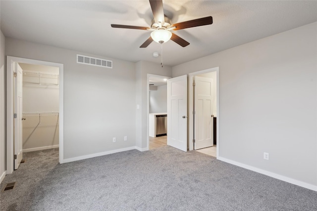 unfurnished bedroom featuring ceiling fan, a spacious closet, light colored carpet, and a closet