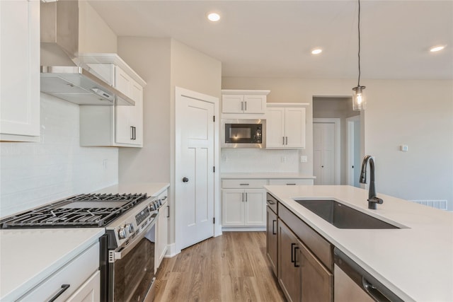 kitchen with wall chimney exhaust hood, stainless steel appliances, sink, white cabinetry, and hanging light fixtures