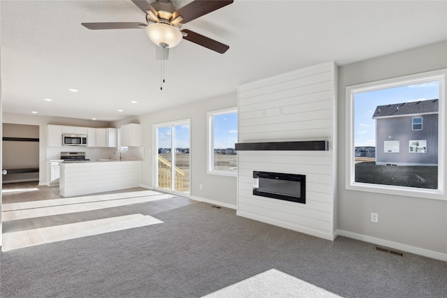 unfurnished living room with carpet floors, sink, a large fireplace, and ceiling fan