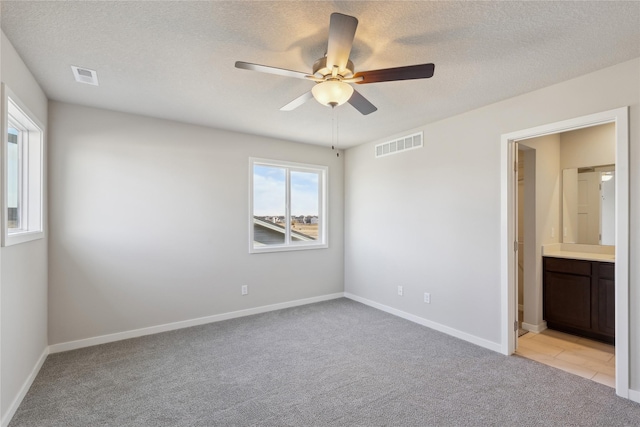 unfurnished bedroom featuring ceiling fan, light colored carpet, multiple windows, and ensuite bathroom