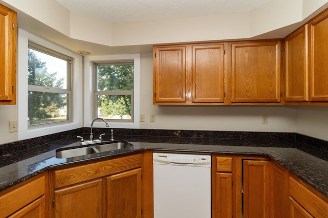 kitchen featuring dark stone counters, brown cabinetry, white dishwasher, and a sink