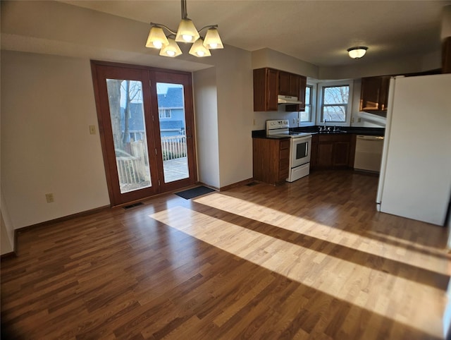 kitchen with white appliances, dark countertops, dark wood-type flooring, and under cabinet range hood