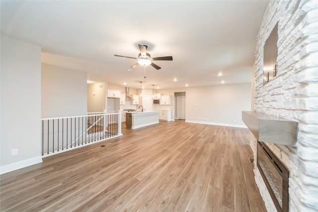 unfurnished living room featuring light hardwood / wood-style floors, sink, ceiling fan, and a fireplace