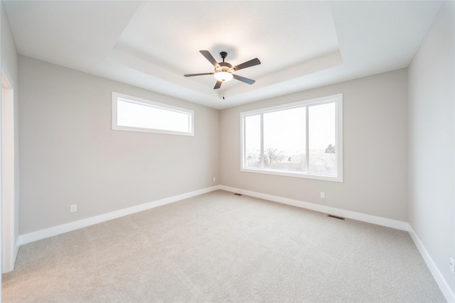 carpeted spare room featuring ceiling fan and a tray ceiling