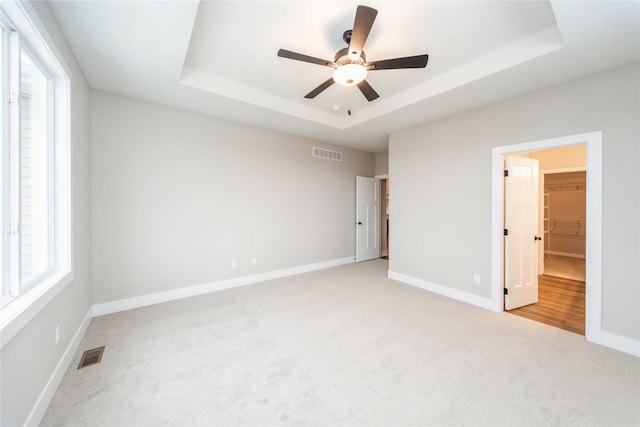 unfurnished bedroom featuring a walk in closet, a closet, light colored carpet, ceiling fan, and a tray ceiling