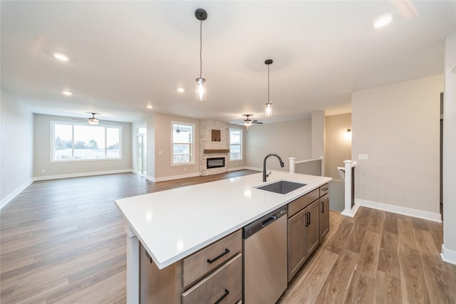 kitchen with dishwasher, hanging light fixtures, sink, a stone fireplace, and a kitchen island with sink