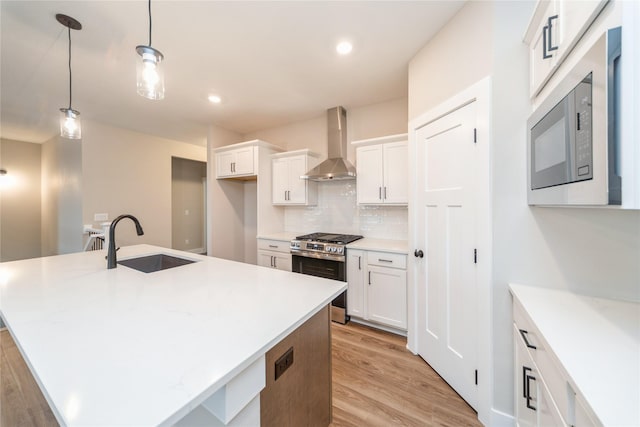 kitchen with gas range, wall chimney range hood, sink, pendant lighting, and a center island with sink