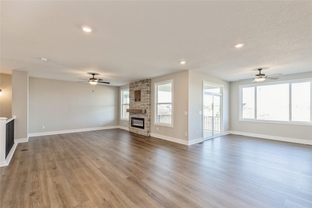 unfurnished living room with hardwood / wood-style flooring, plenty of natural light, ceiling fan, and a stone fireplace