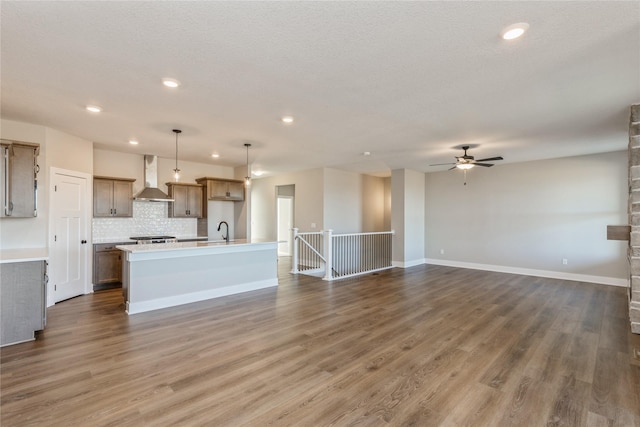 kitchen with a kitchen island with sink, sink, wall chimney exhaust hood, decorative light fixtures, and dark hardwood / wood-style flooring