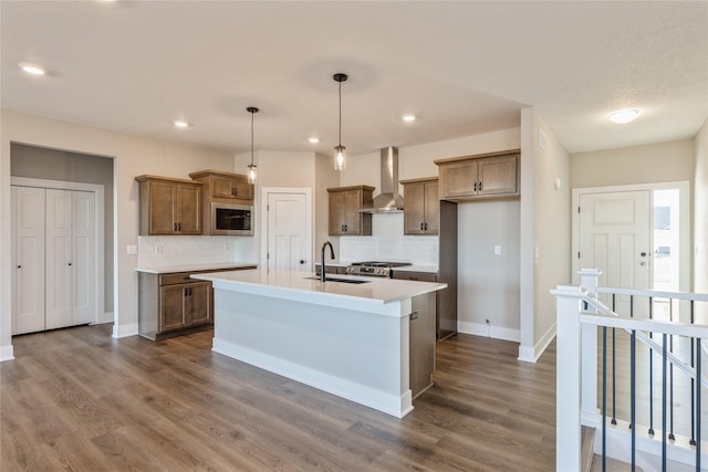 kitchen featuring appliances with stainless steel finishes, wall chimney exhaust hood, sink, a center island with sink, and hanging light fixtures