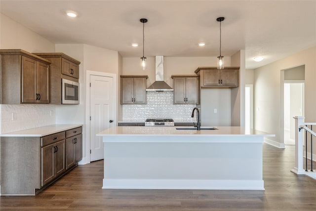 kitchen featuring sink, a kitchen island with sink, hanging light fixtures, and wall chimney range hood