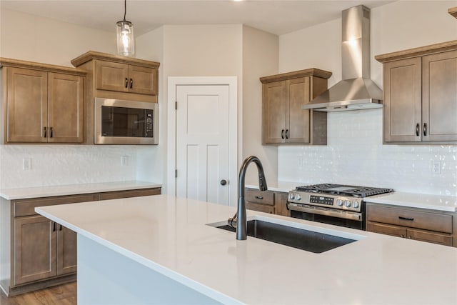 kitchen with sink, stainless steel appliances, wall chimney range hood, a kitchen island with sink, and light wood-type flooring