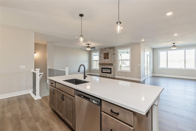 kitchen featuring dishwasher, a center island with sink, sink, decorative light fixtures, and light hardwood / wood-style floors