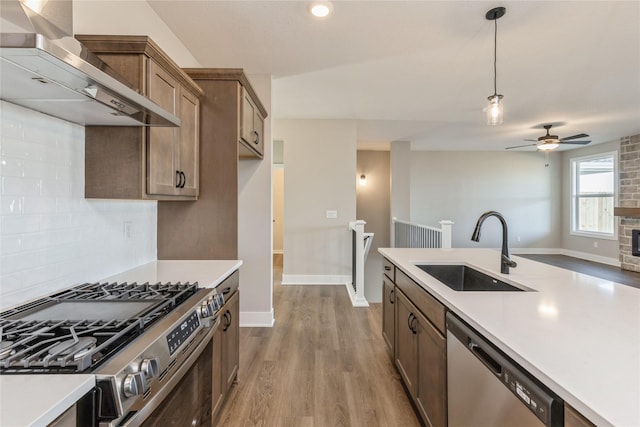 kitchen with sink, wall chimney exhaust hood, pendant lighting, appliances with stainless steel finishes, and light wood-type flooring