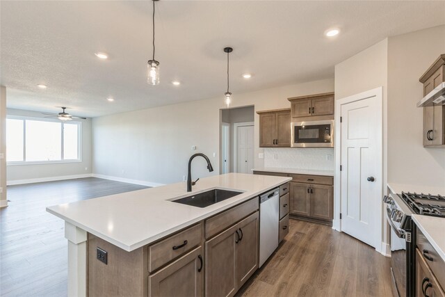 kitchen featuring stainless steel appliances, ceiling fan, sink, hanging light fixtures, and an island with sink