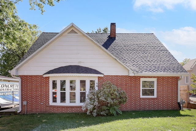 back of property featuring a yard, roof with shingles, a chimney, and brick siding